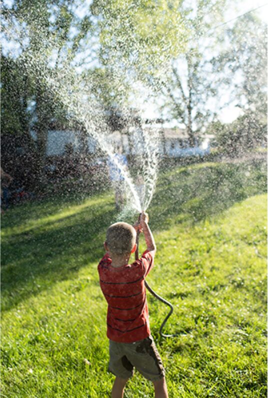 Boy spraying a garden hose into the air on a sunny lawn