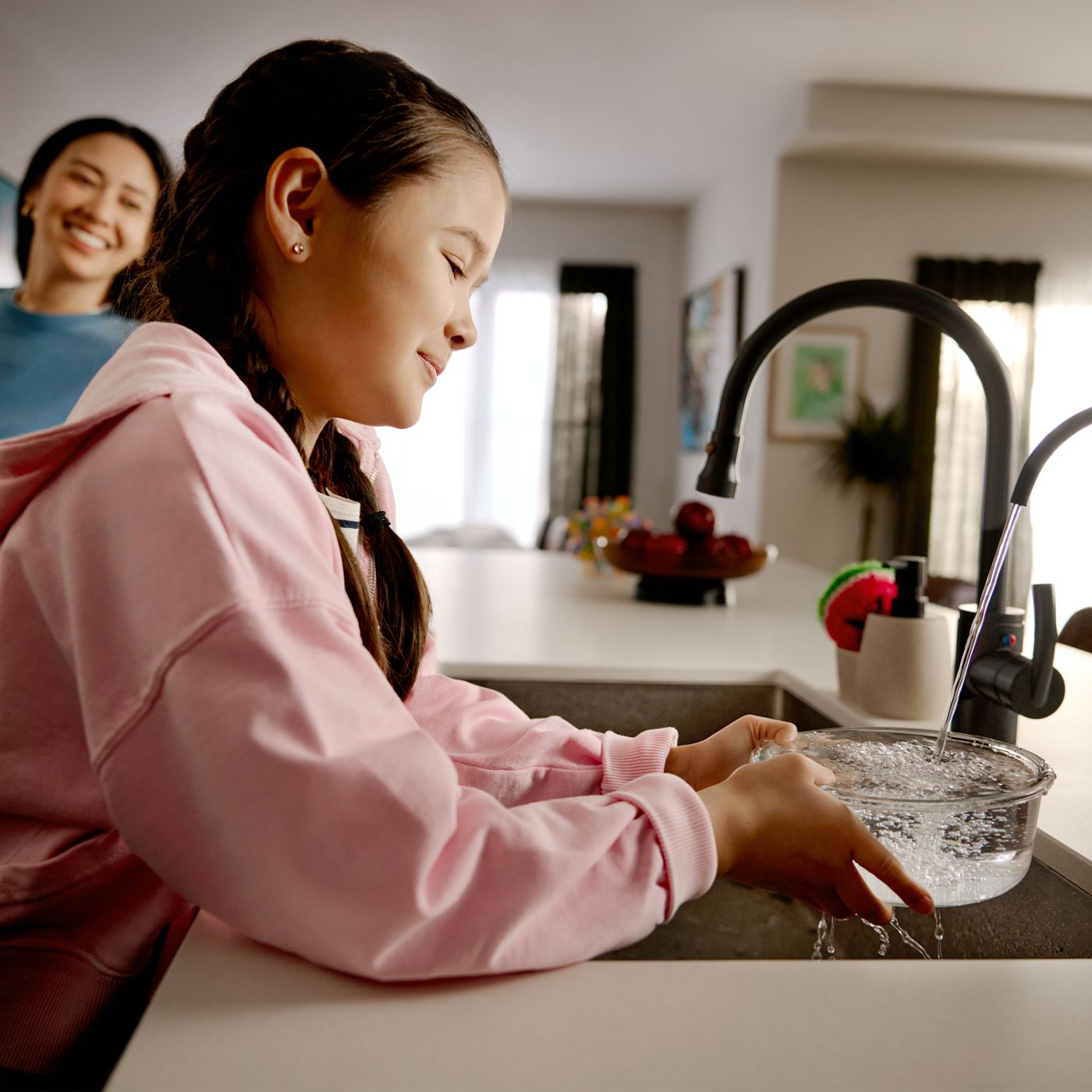 A girl rinsing a glass bowl at the kitchen sink