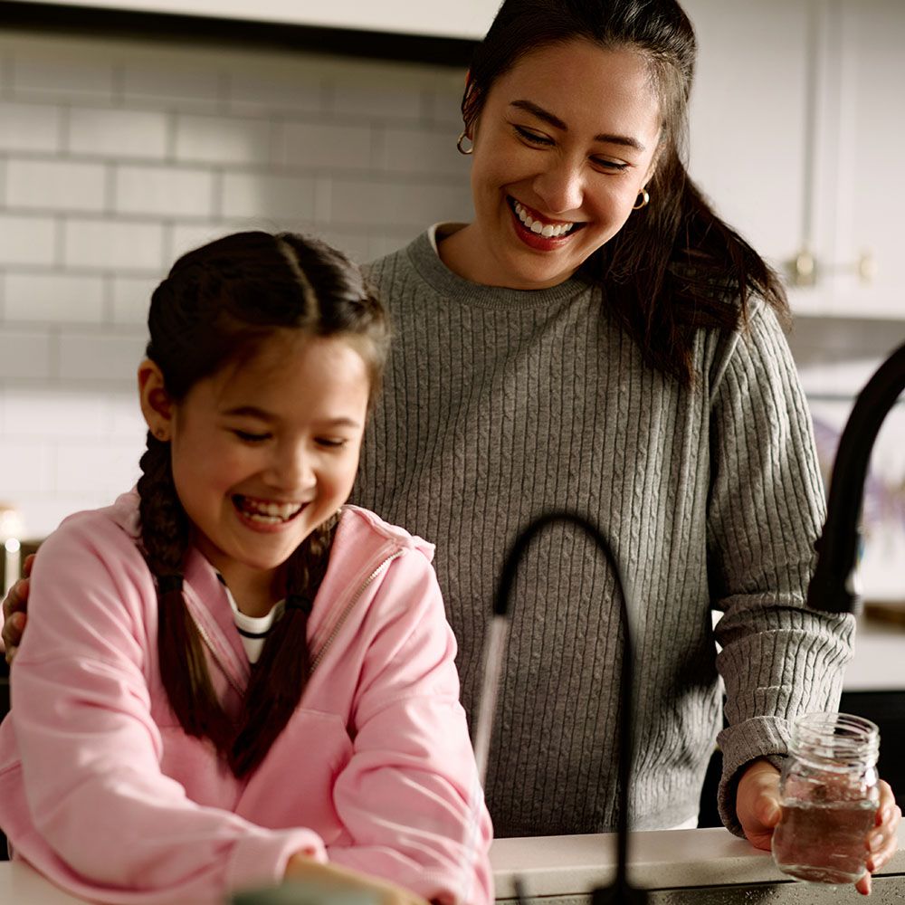 A mother and daughter laughing at the kitchen sink