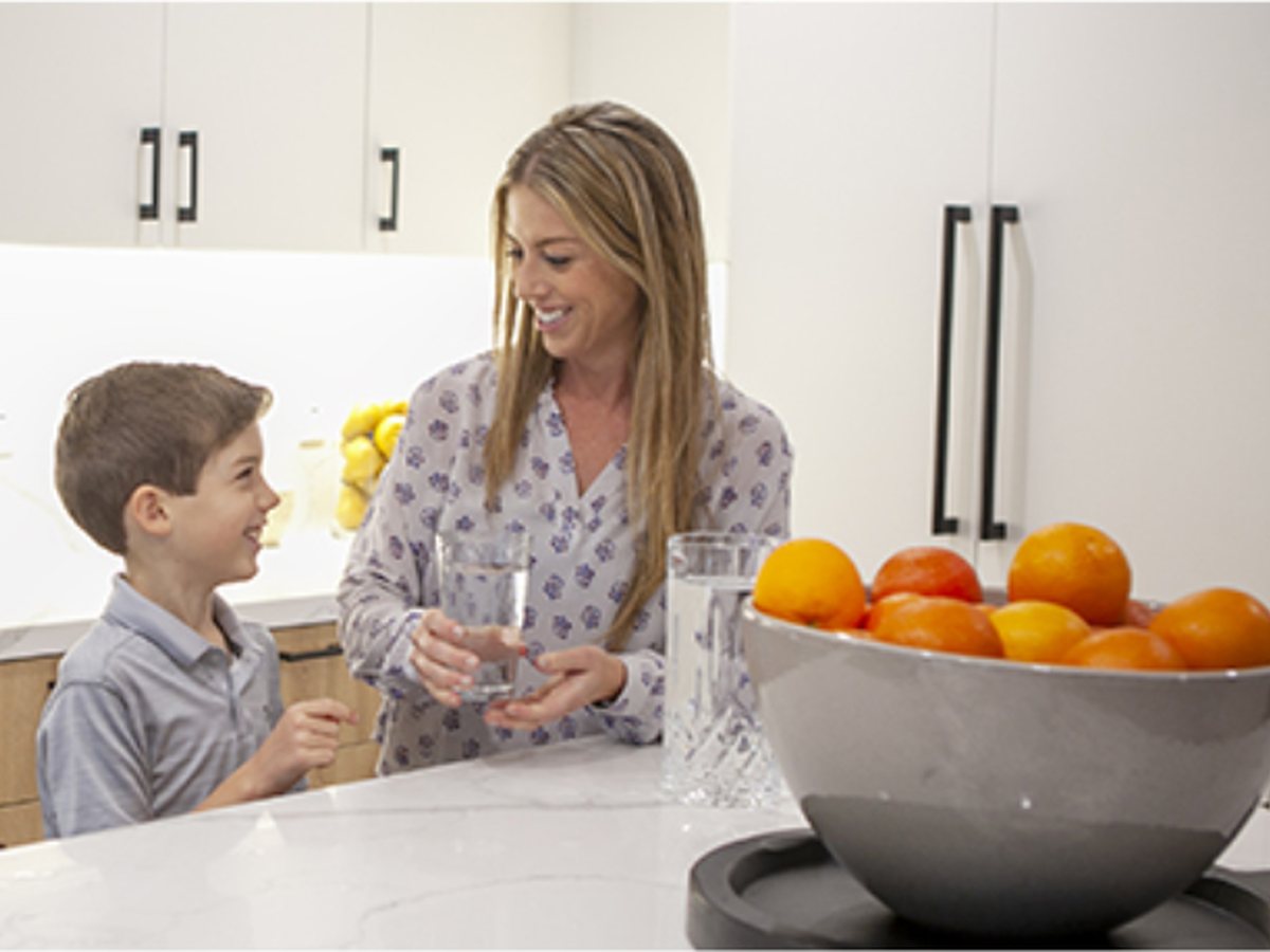 A mother handing her son a glass of water at the kitchen island