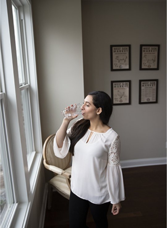A woman drinking a glass of water by a bright window