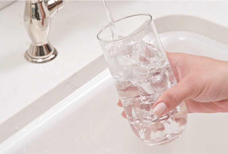 Hand holding a glass of ice water at the kitchen sink