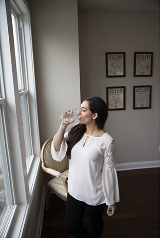 Woman drinking a glass of water by a bright window in the early morning